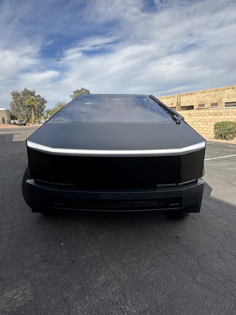 A black car parked in the street with a building behind it.